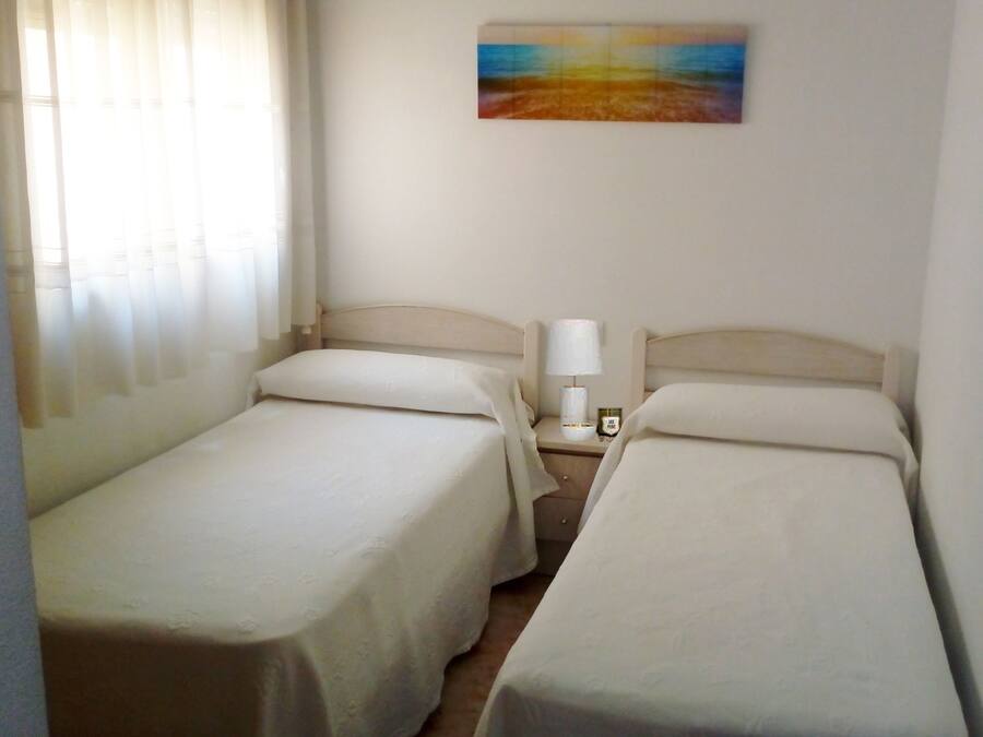 A hotel room with two single beds, a nightstand with a lamp, and a painting on the wall.
