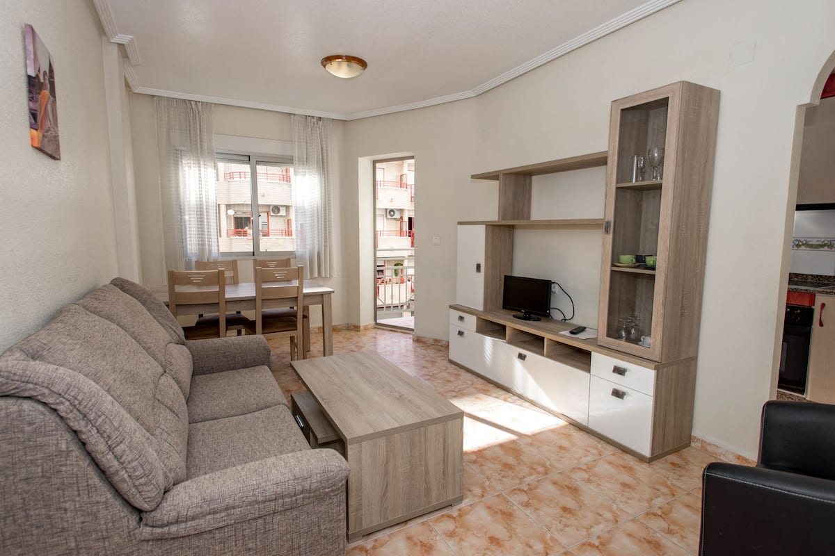 A living room with a sofa, TV stand, and dining area.