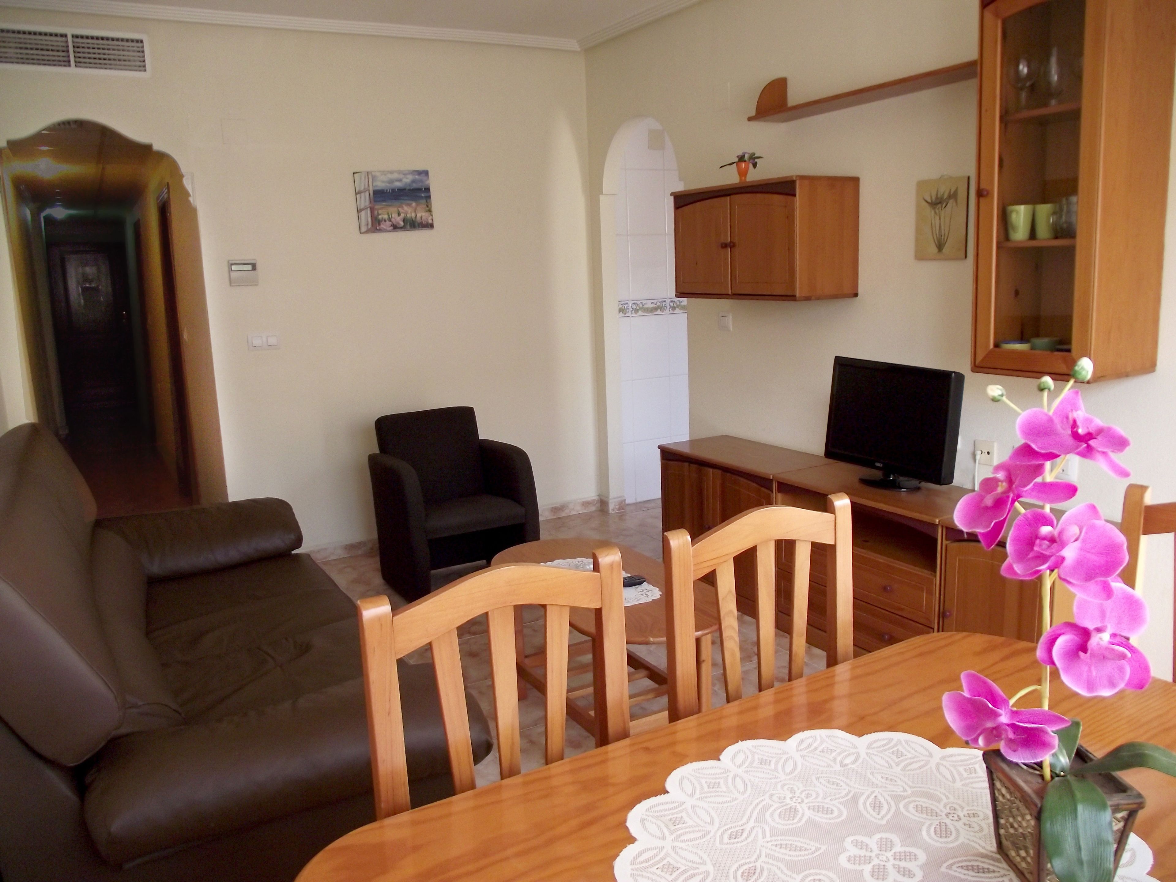 A living room with a sofa, chairs, a wooden table, a TV, and a cabinet with decorative items.