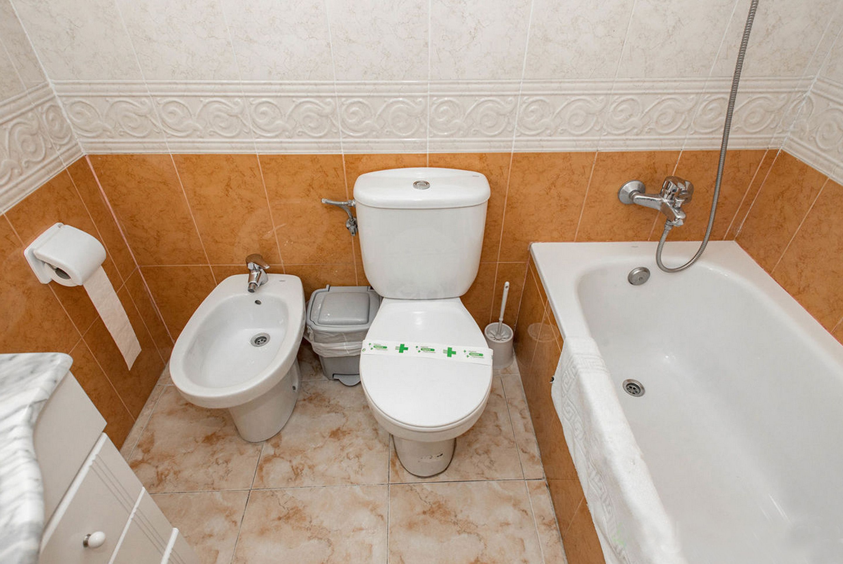 Een badkamer met toilet, bidet, prullenbak en bad.