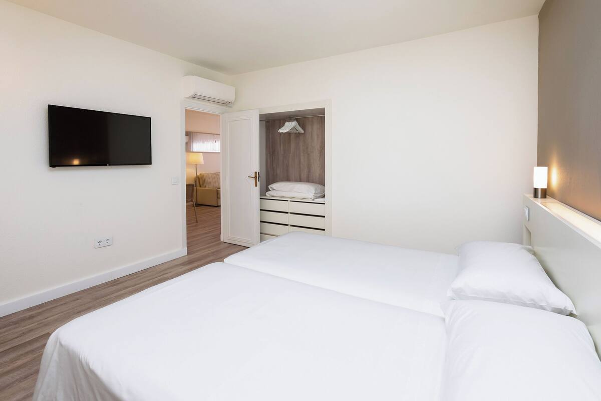 Habitación de hotel con una cama, un televisor montado en la pared y un vestidor con perchero.