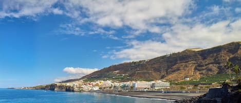 A coastal town with buildings along the shoreline, a beach, and a mountainous backdrop.