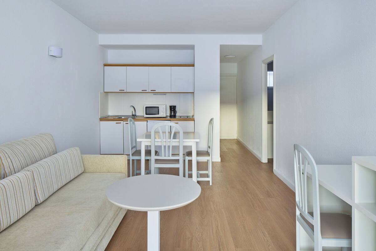 Una sala de estar moderna con un sofá, una mesa redonda y una zona de cocina con armarios y un microondas.