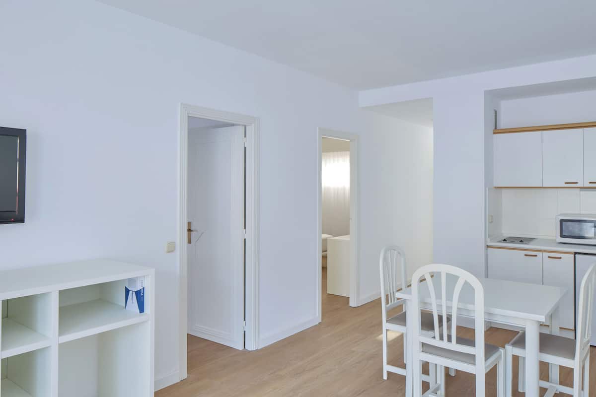 Un apartamento moderno con una decoración blanca, que incluye cocina, comedor y televisor montado en la pared.