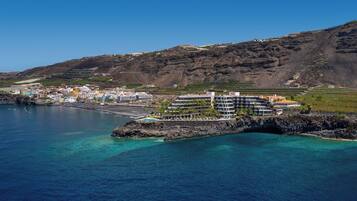 A coastal town with a prominent hotel featuring multiple floors, a beach, and clear blue waters.