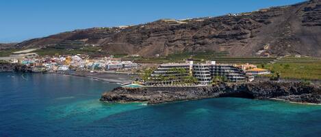 A coastal town with a prominent hotel featuring multiple floors, a beach, and clear blue waters.
