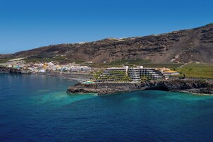 A coastal town with a prominent hotel featuring multiple floors, a beach, and clear blue waters.