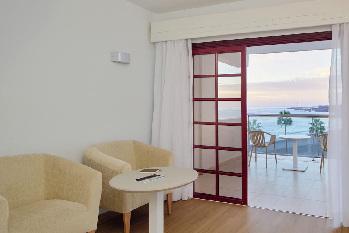 Una habitación con dos sillones color beige, una mesita redonda y vista al mar a través de un ventanal.