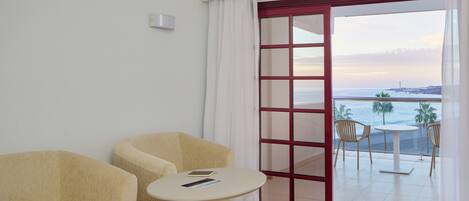 A room with two beige armchairs, a small round table, and a view of the sea through a glass door.