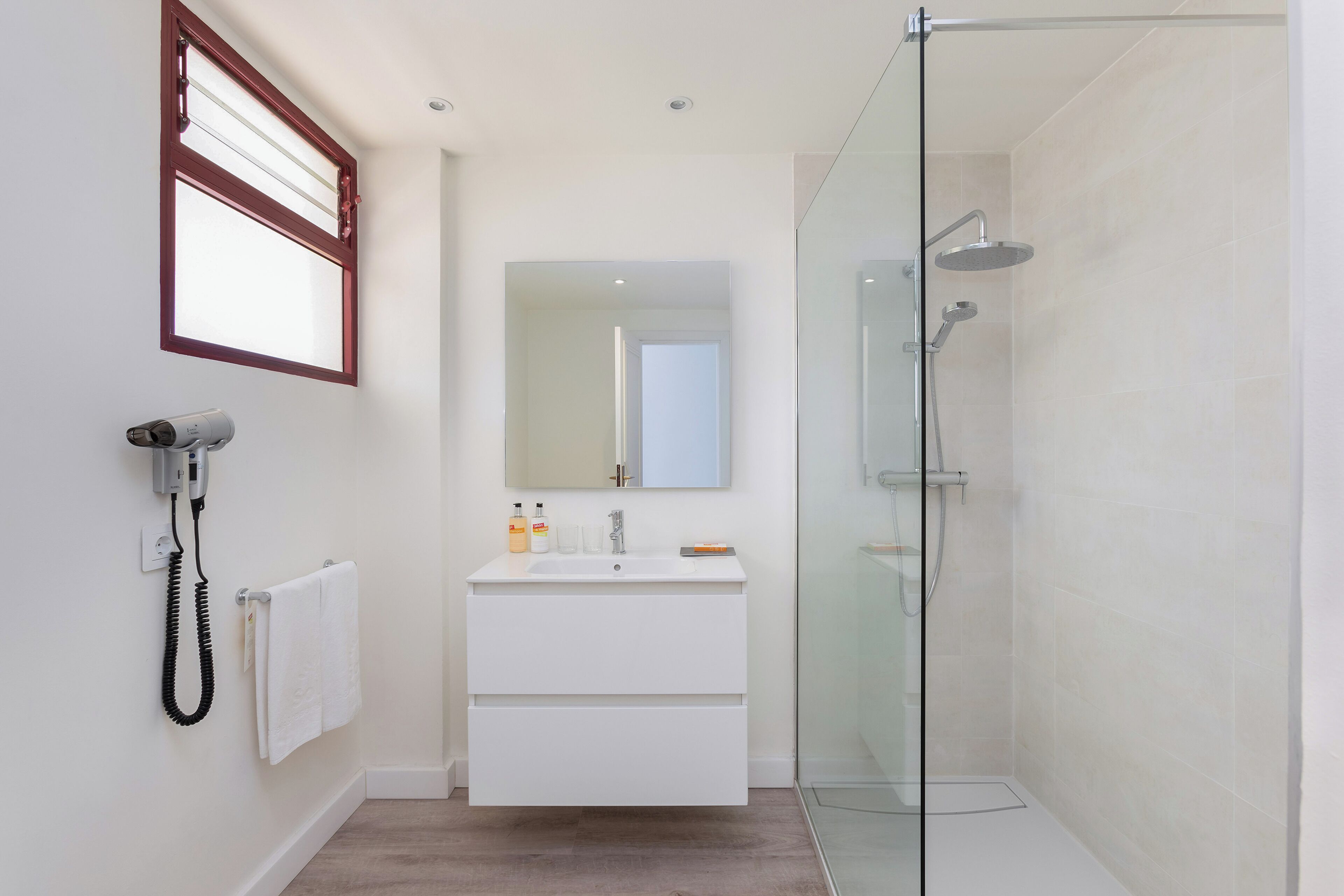 Une salle de bain moderne avec une douche à parois de verre, un meuble-lavabo blanc avec un miroir et un sèche-cheveux fixé au mur.