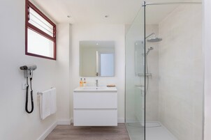 A modern bathroom with a glass-enclosed shower, a white vanity with a mirror, and a hairdryer on the wall.