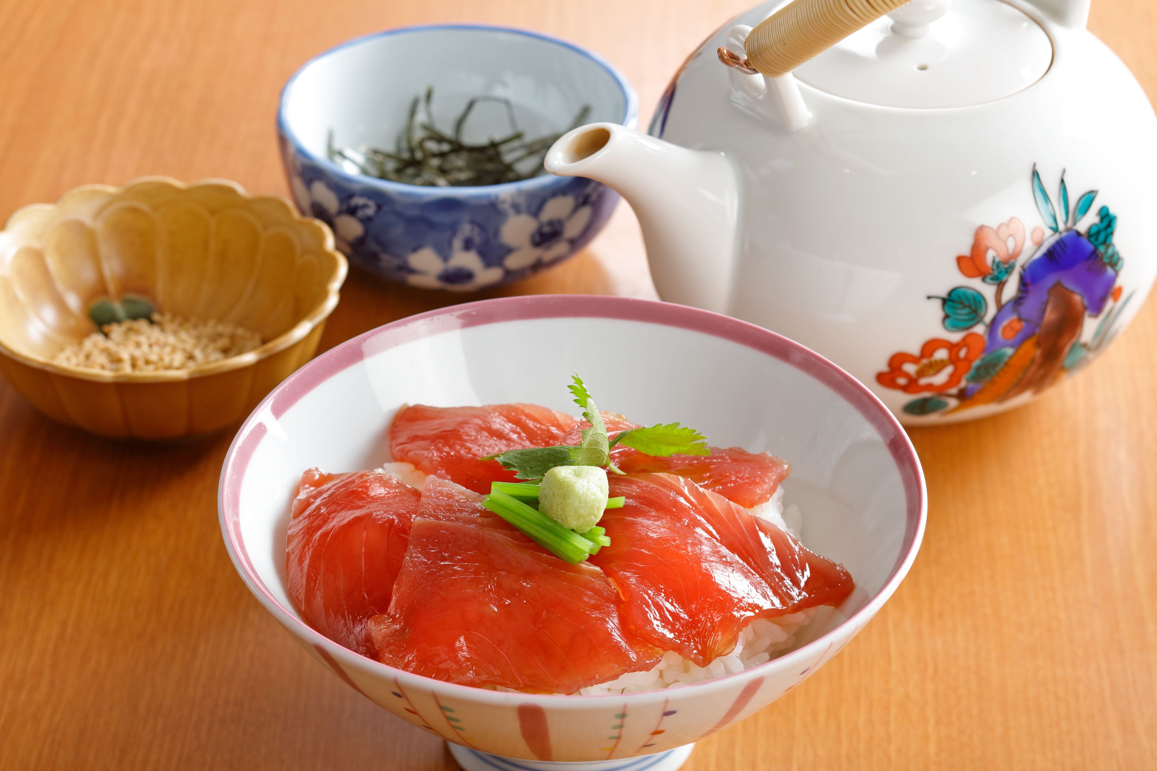 A bowl of sashimi with rice, a teapot, and a bowl of green tea.