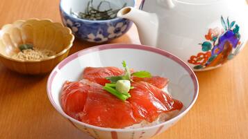 A bowl of sashimi with rice, a teapot, and a bowl of green tea.