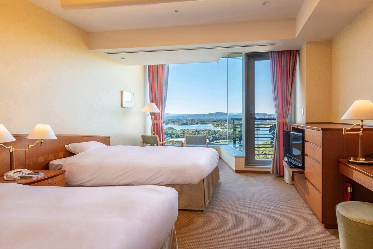 Une chambre d’hôtel avec deux lits, une télévision, un bureau avec une lampe et une vue sur un paysage.