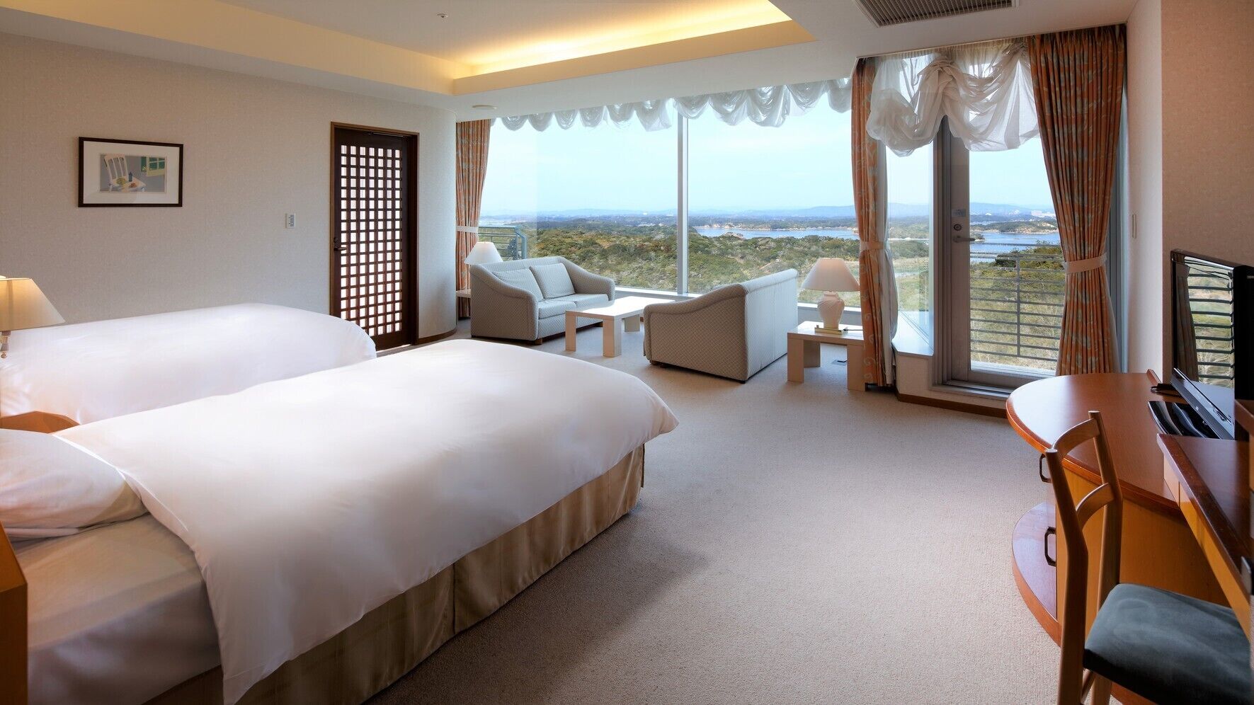 Ein Hotelzimmer mit einem großen Bett, einer Sitzecke, einem Schreibtisch und Blick ins Freie.