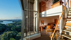Een modern interieur met een balkon, een trap en uitzicht op een bebost gebied.