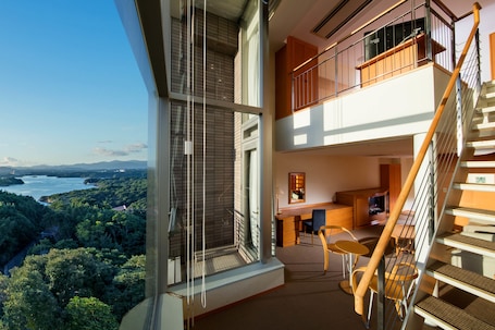A modern interior with a balcony, a staircase, and a view of a forested area.