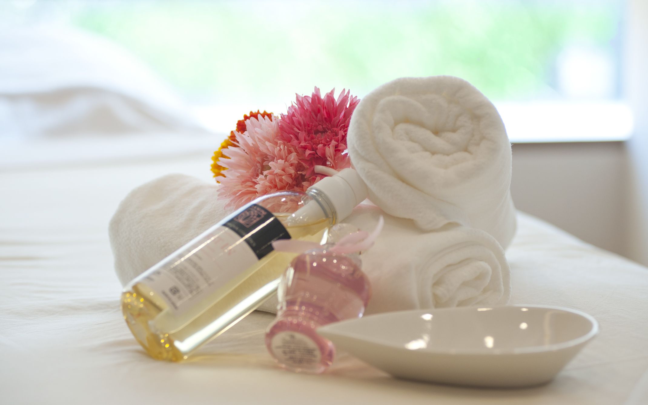 A neatly arranged bathroom with a white towel, a bottle of lotion, a pink bottle, and a bowl on a white surface.