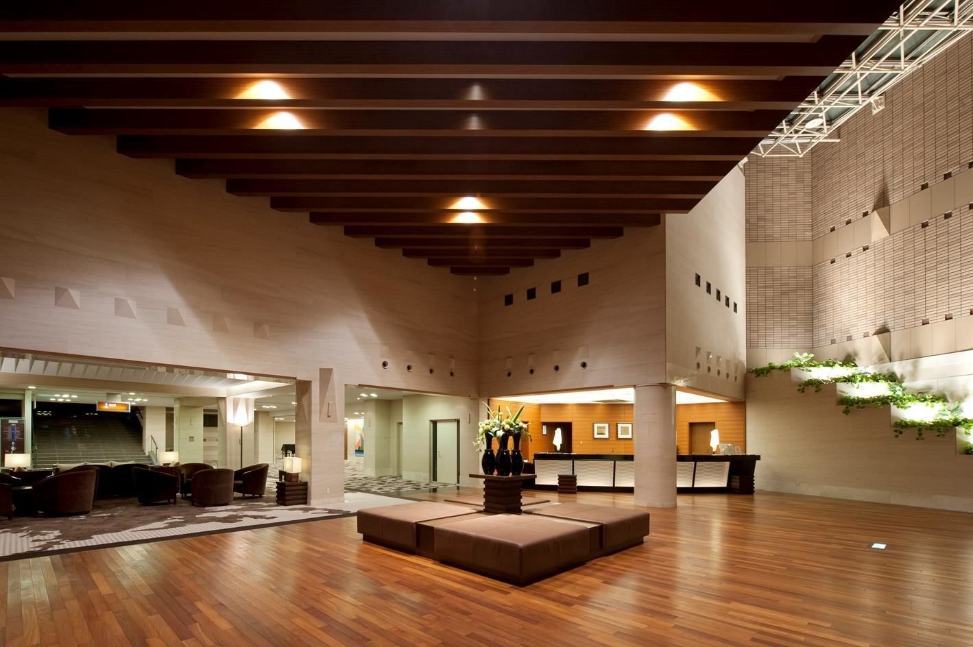 A spacious lobby with a wooden floor, a central seating area, and a high ceiling with exposed beams.