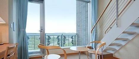 Una habitación con un gran ventanal, una escalera y dos mesas redondas con sillas.