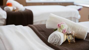 Habitación de hotel con dos camas, cada una cubierta con toallas blancas y marrones, y una pequeña botella de perfume sobre la cama.