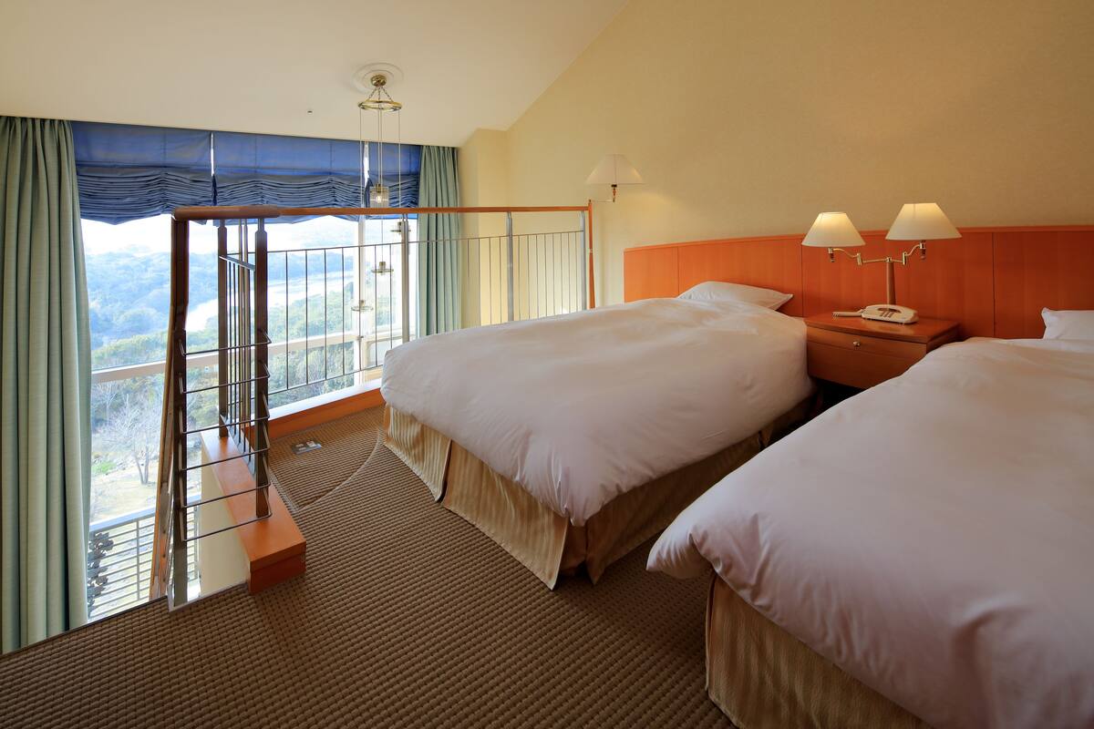 Une chambre d’hôtel avec deux lits, un balcon offrant une vue et une tête de lit en bois.
