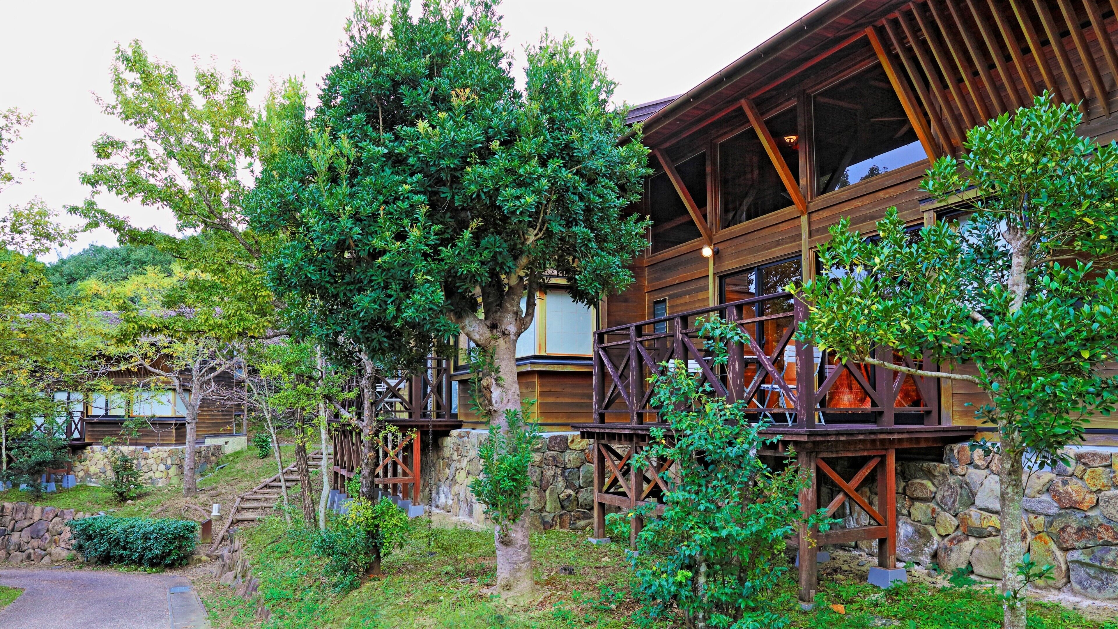 Un bâtiment en bois avec un mur en pierre, une terrasse en bois et un escalier menant à l’entrée.