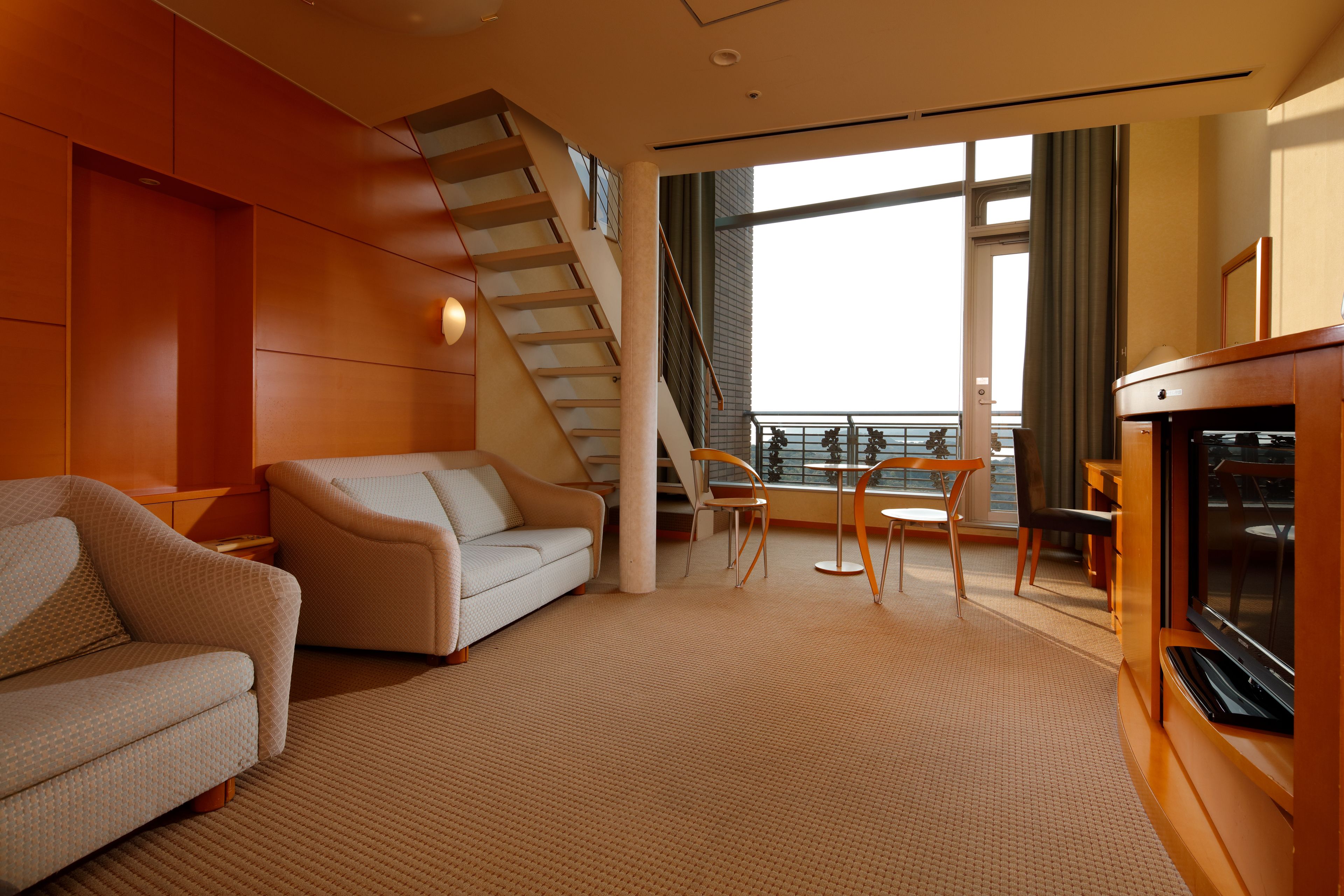 A modern living room with a sofa, a coffee table, and a fireplace. There is a staircase leading to an upper level.
