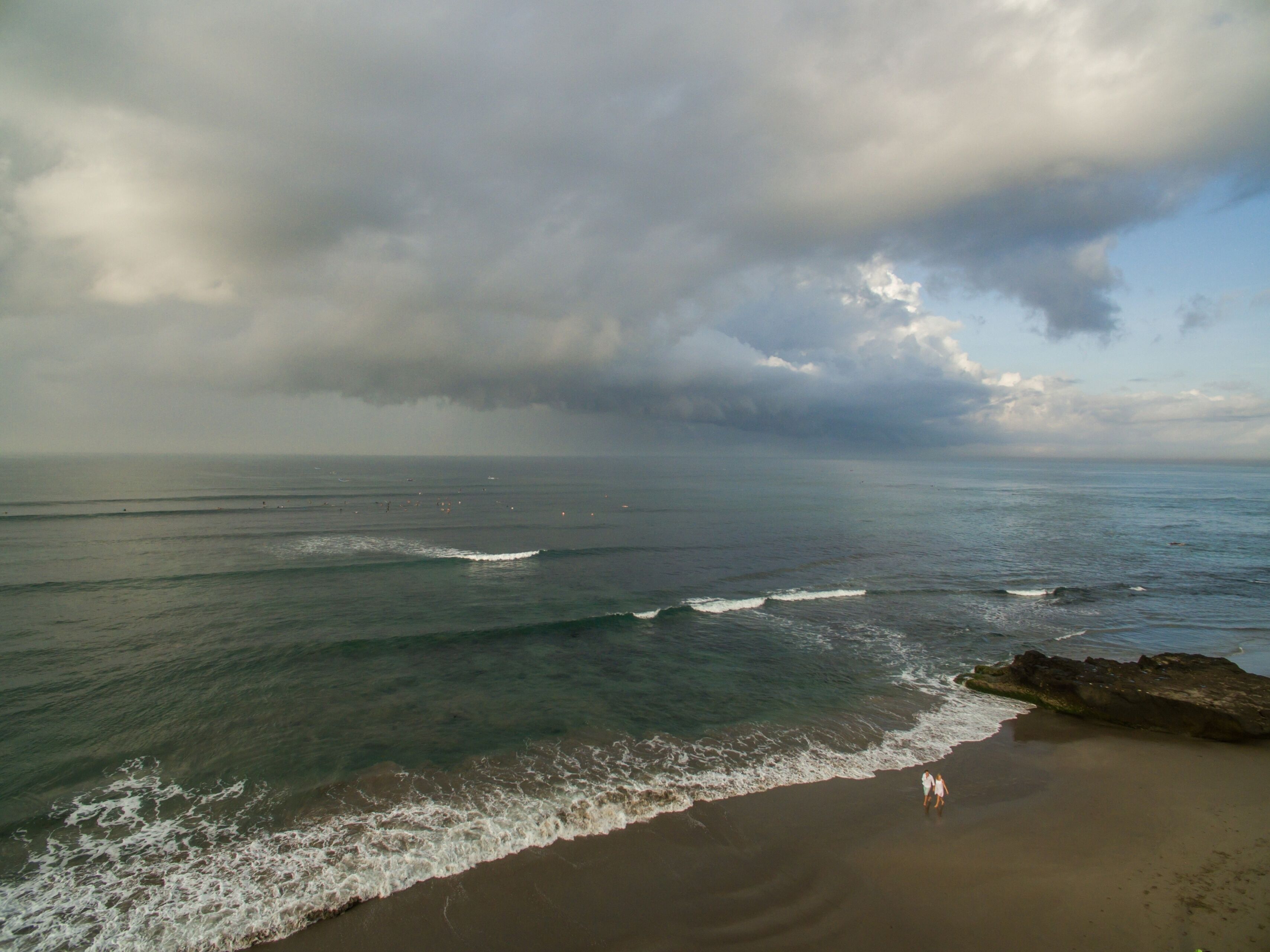 A beach with waves, a cloudy sky, and a rocky outcrop.
