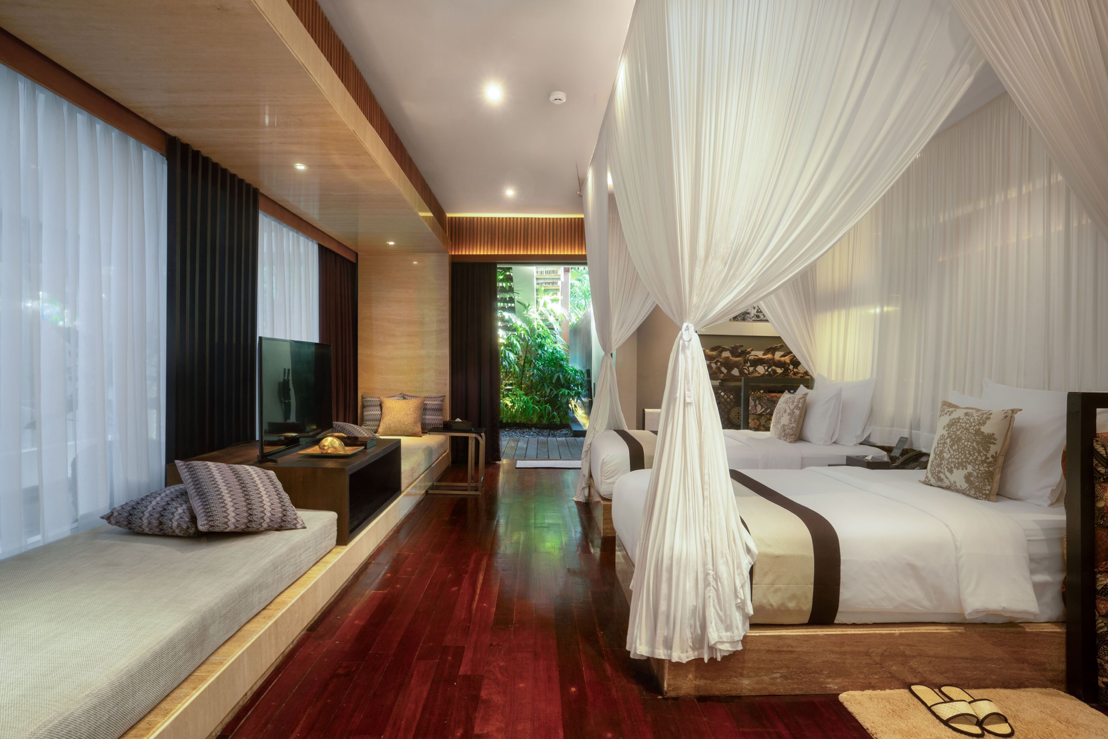 A modern bedroom with a bed, a sofa, a TV, and a view of greenery.