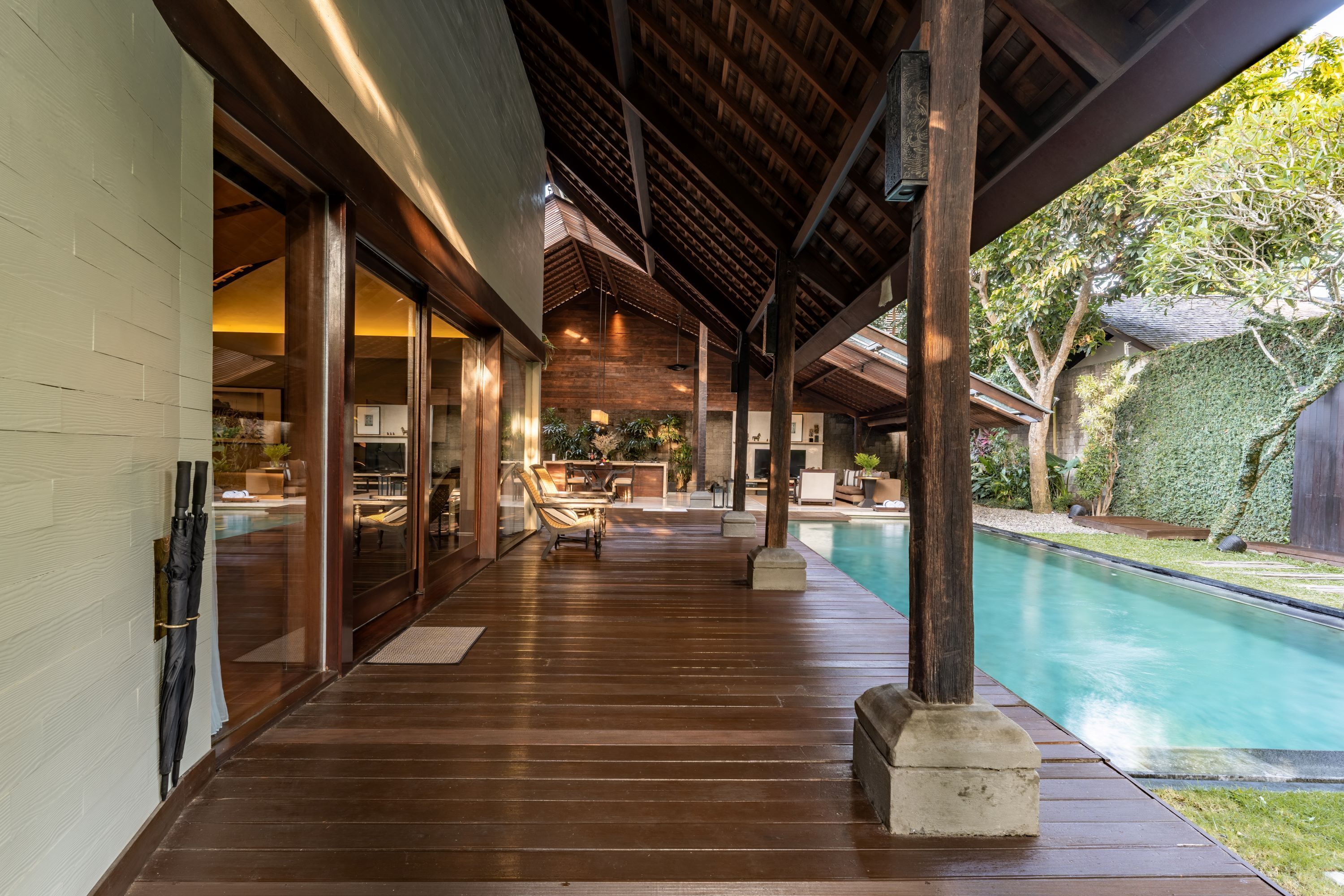 A covered outdoor area with a pool, wooden flooring, and a view of the backyard.