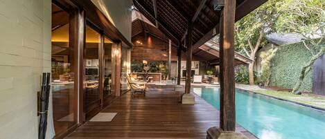 A covered outdoor area with a pool, wooden flooring, and a view of the backyard.