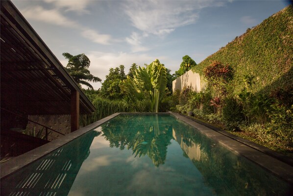 A swimming pool with a clear view of the surrounding greenery and a building on one side. - Ametis Villas (Canggu)