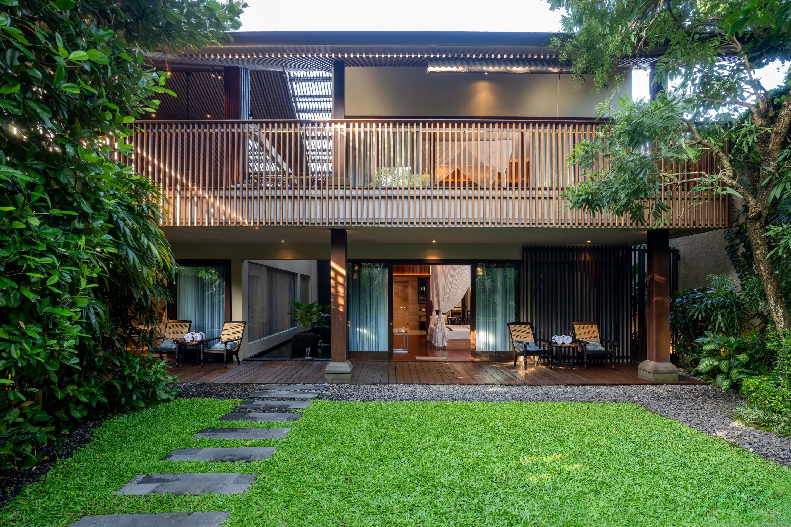 A modern two-story house with a balcony, a staircase, and a well-maintained garden.
