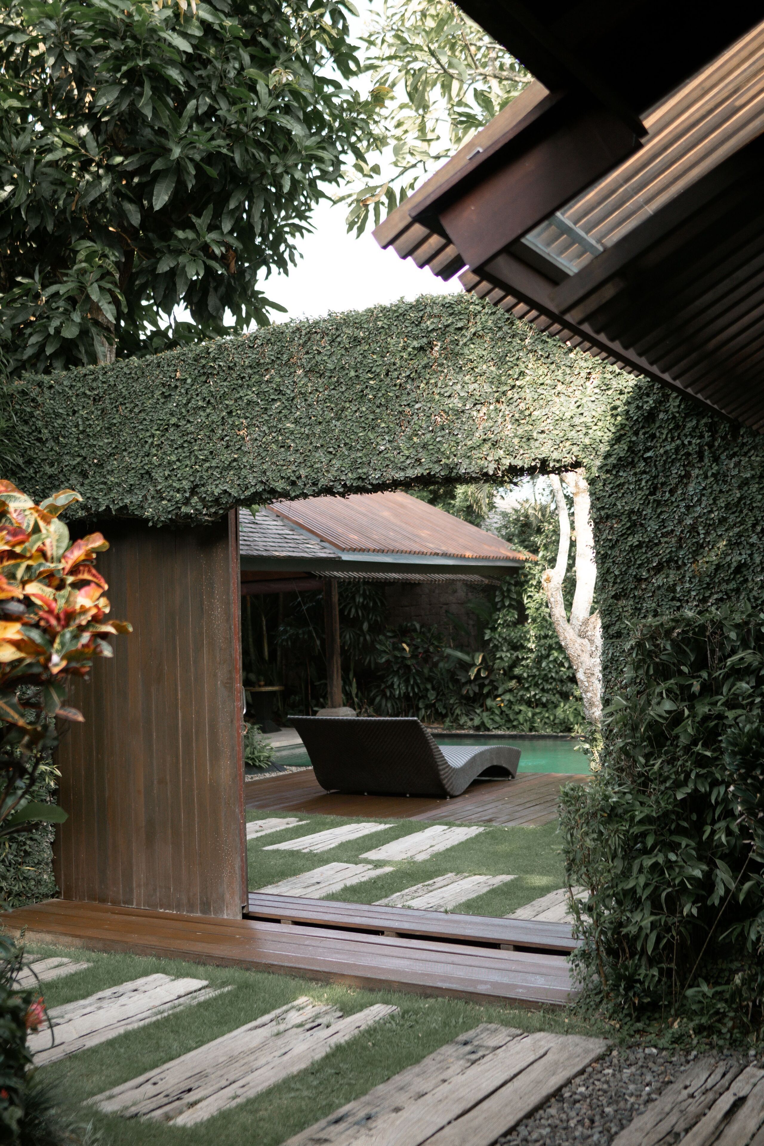 A wooden deck with a pool table, surrounded by lush greenery and a covered seating area.