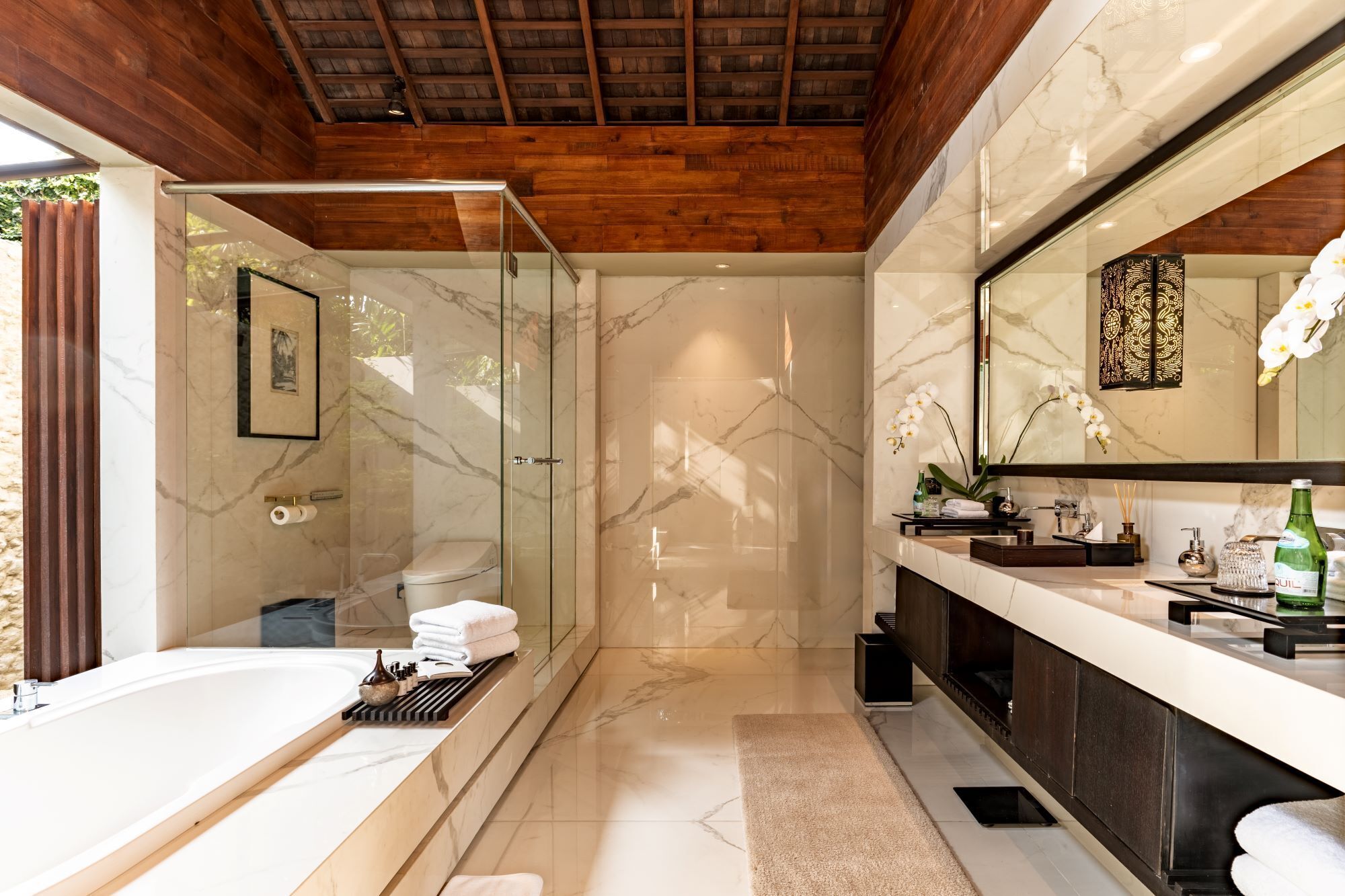 A modern bathroom with a glass shower, a bathtub, a vanity with a large mirror, and marble flooring.