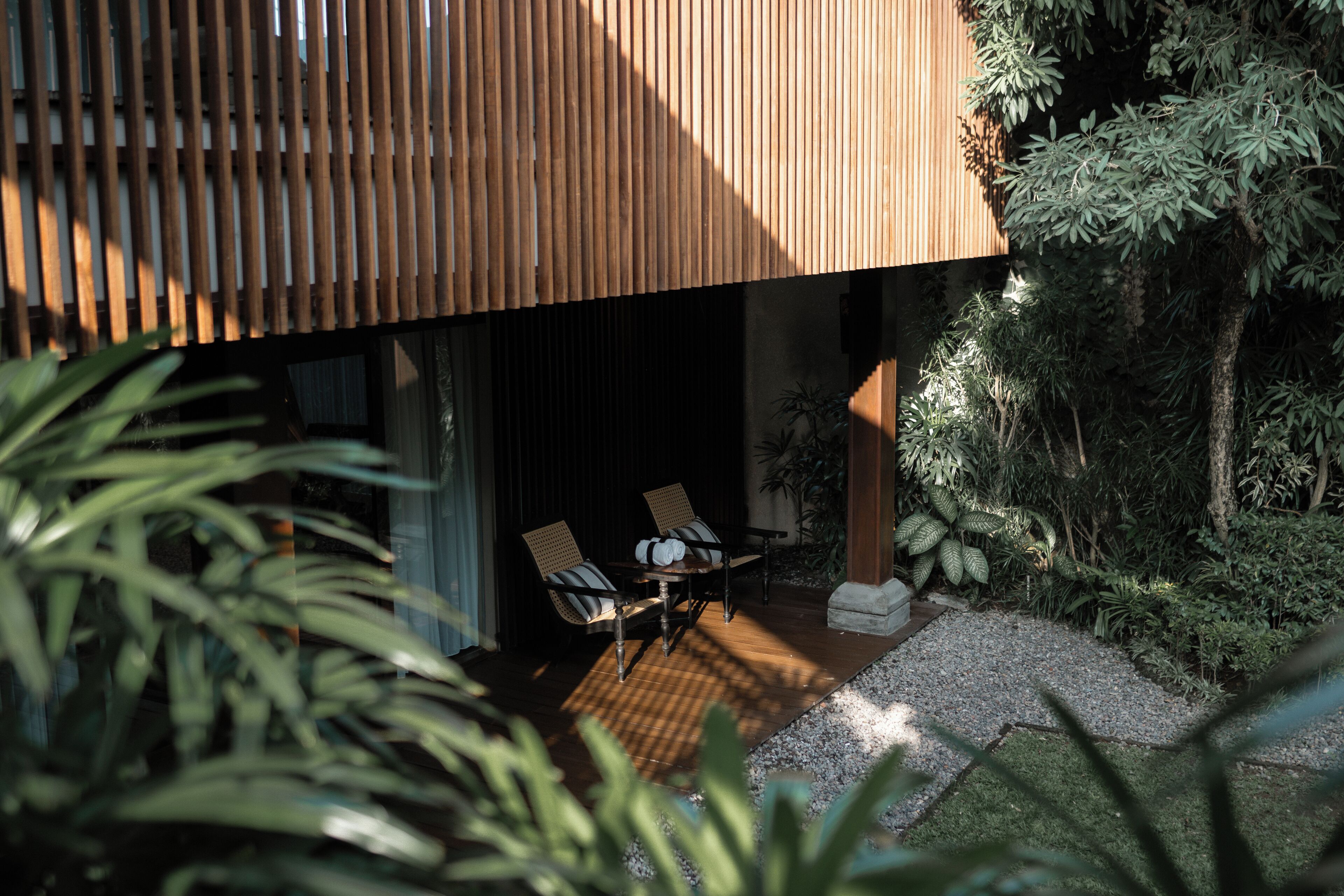 A modern building with a wooden slatted facade, a patio with a table and chairs, and surrounding greenery.