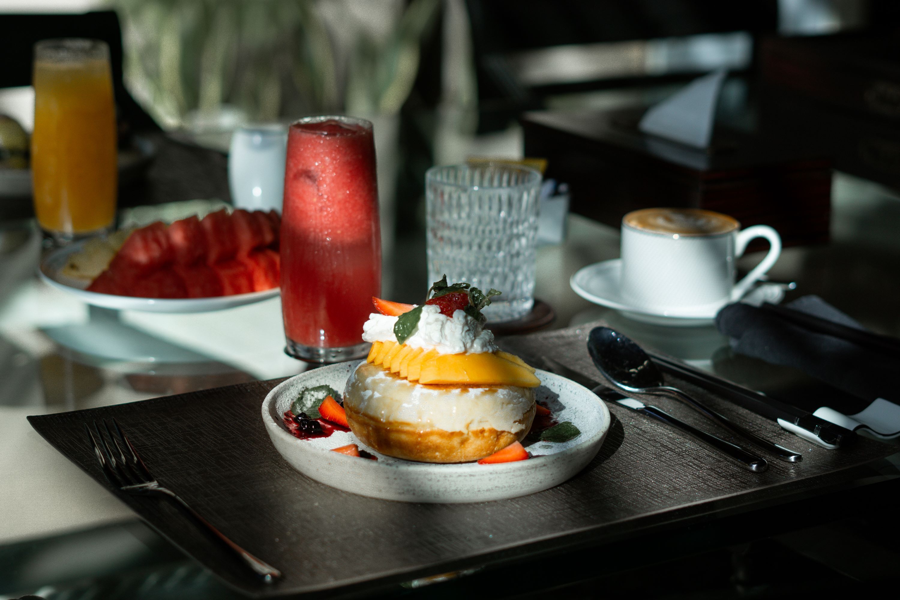 A dessert plate with a fruit-topped pastry, a glass of orange juice, and a cup of coffee on a table.