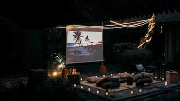 A serene outdoor seating area with a projector displaying a beach scene, surrounded by candles and ambient lighting.
