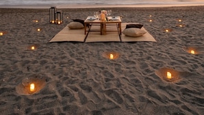 A beach setting with a table set for two, surrounded by candles.