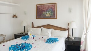 A hotel room with a bed, two bedside tables, a nightstand, a wooden headboard, a painting on the wall, and a door. - Azul Sirena (Santa María Huatulco)