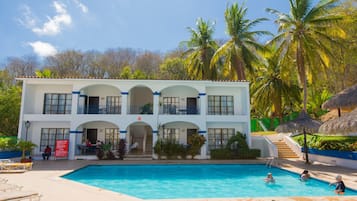 A two-story hotel with a swimming pool, outdoor seating, and palm trees.
