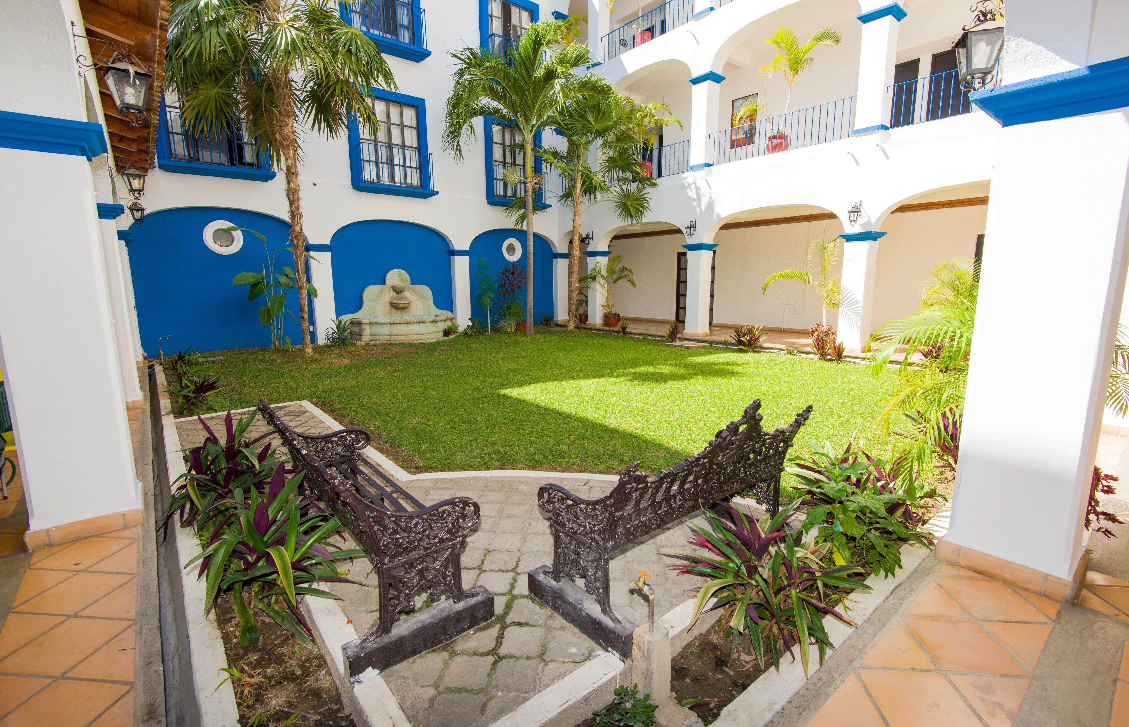 A courtyard with a well-maintained lawn, palm trees, and a stone fountain.