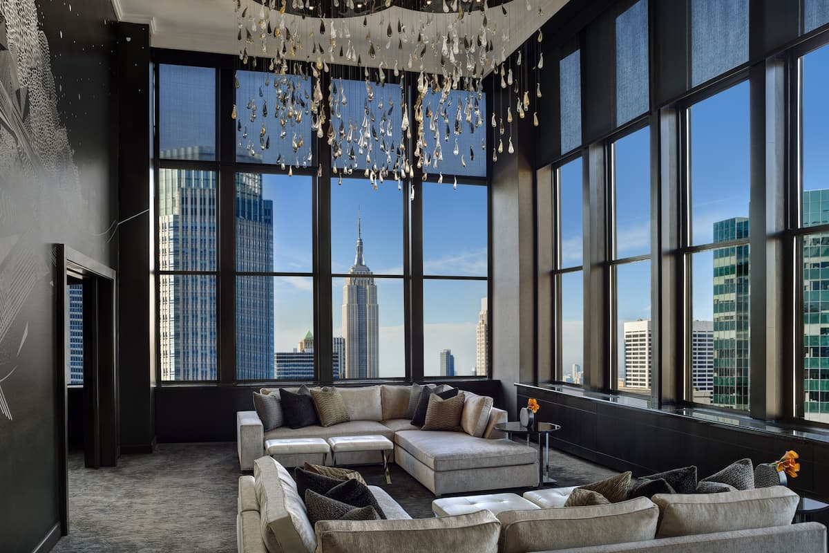 A modern living room with a large sectional sofa, a chandelier, and a city view through large windows.
