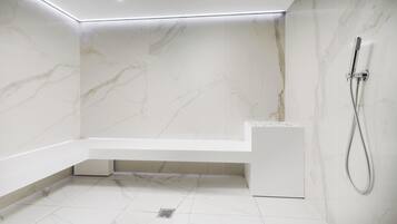 A modern bathroom with a marble wall, a built-in bathtub, and a showerhead.