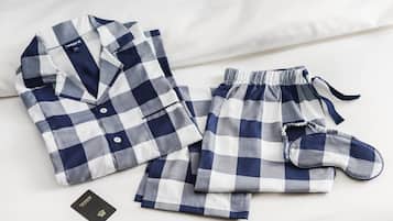 Un conjunto de pijama azul y blanco a cuadros, impecablemente doblado, que incluye una camisa, pantalón y antifaz, sobre una cama.