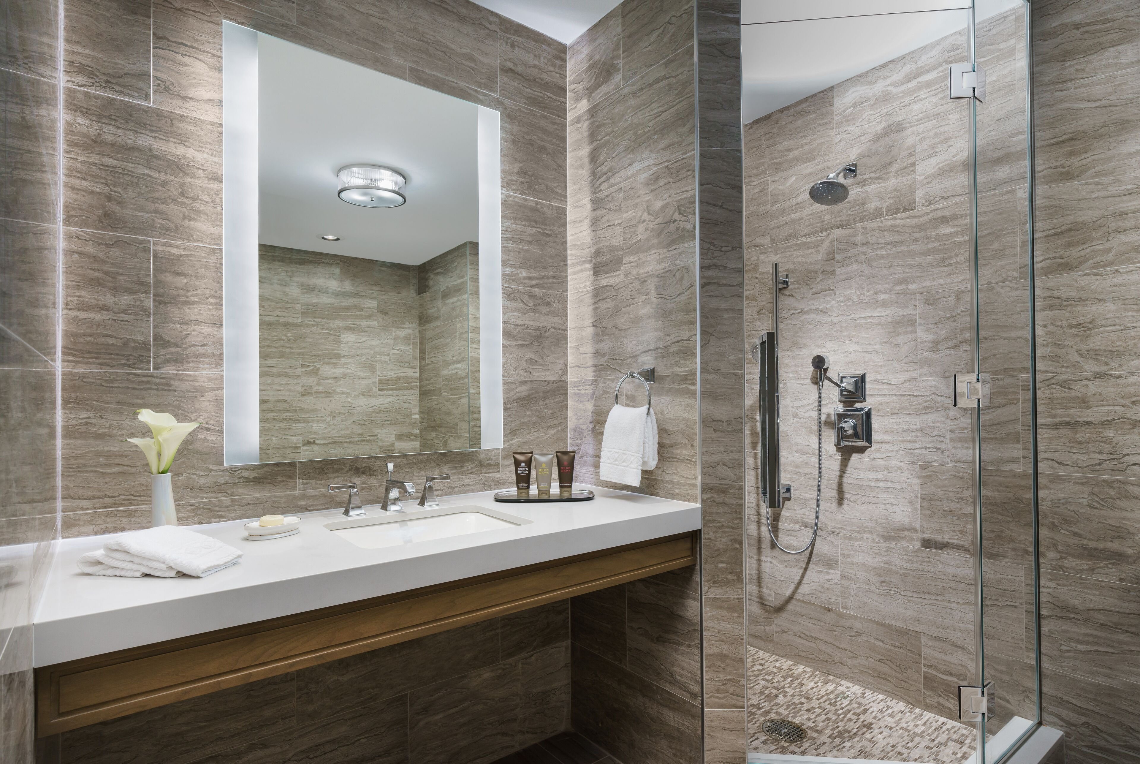 A modern bathroom with a large mirror, a sink, and a glass-enclosed shower.