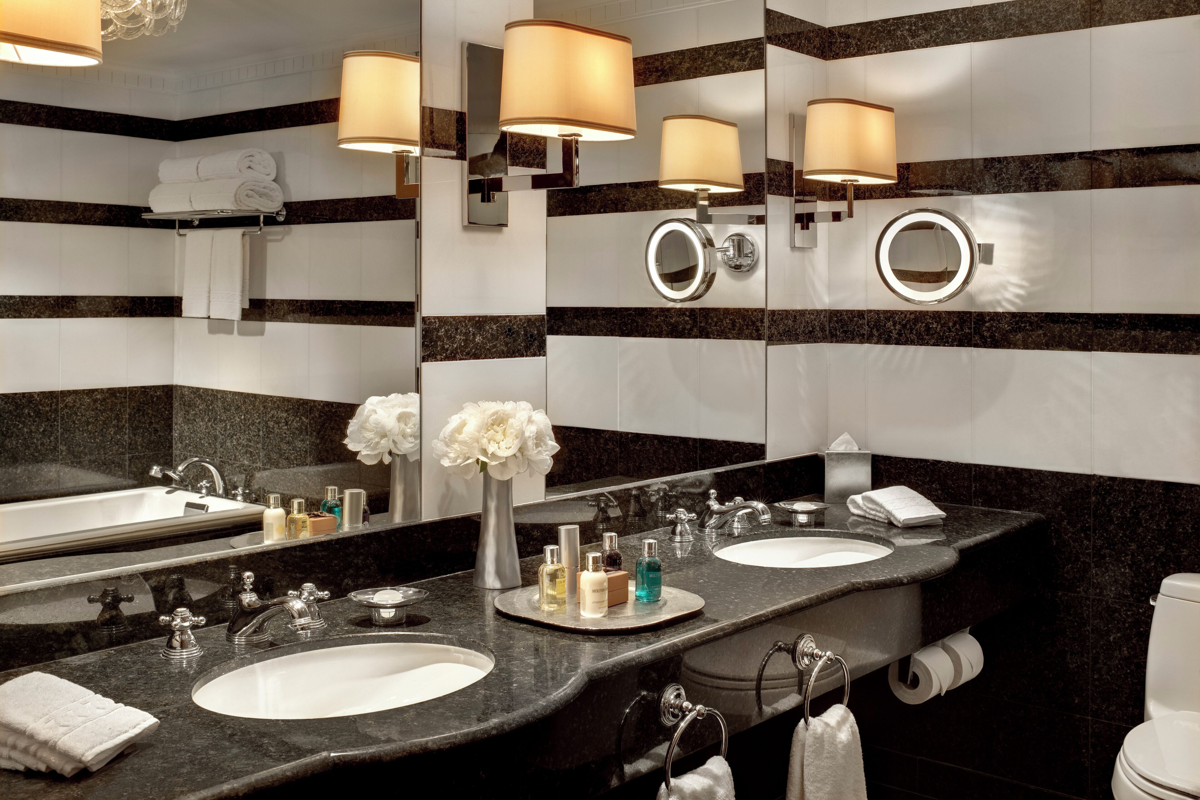 A bathroom with two sinks, a large mirror, wall-mounted lamps, and a toilet.