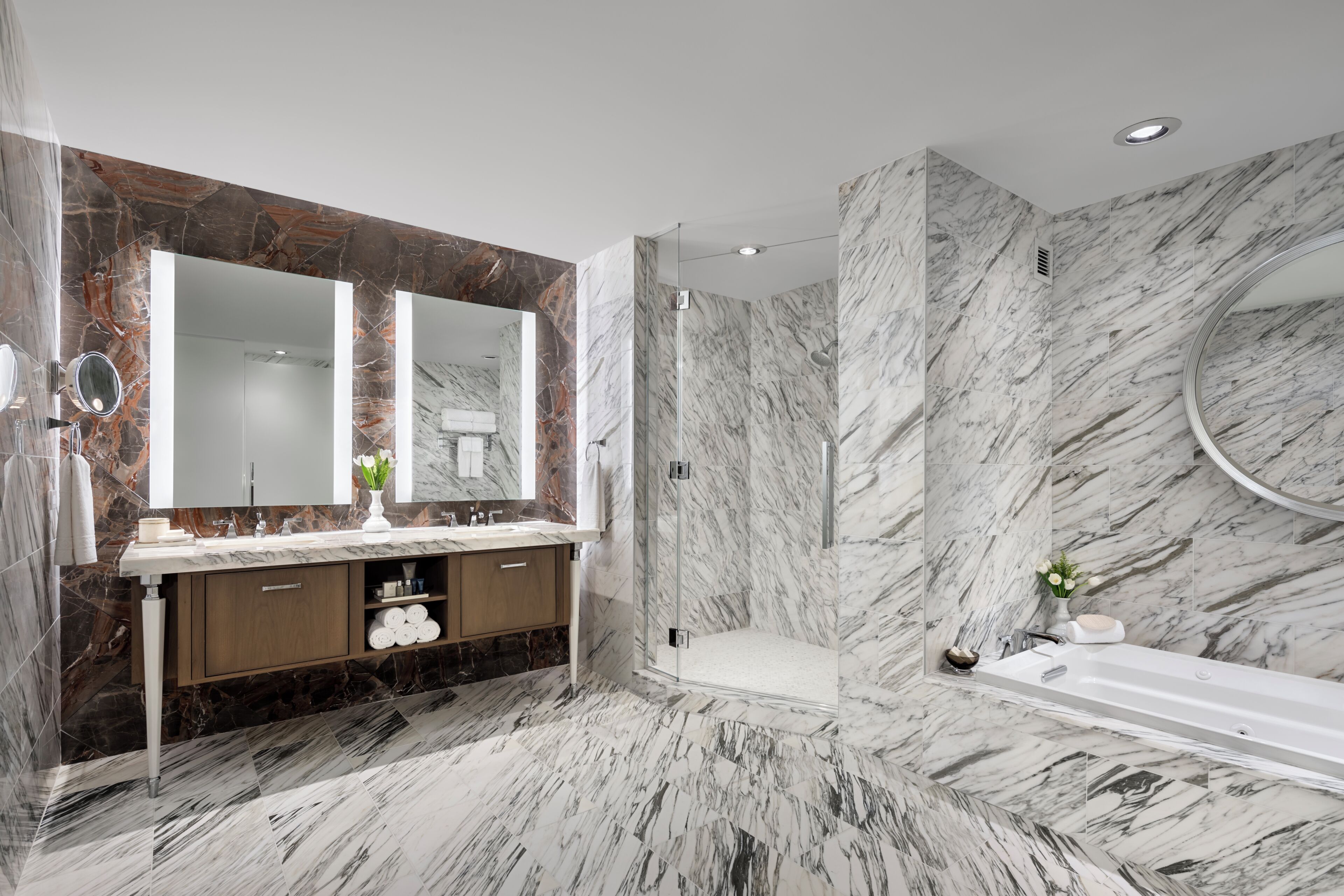 A modern bathroom with a large mirror, dual sinks, a shower, and marble flooring.