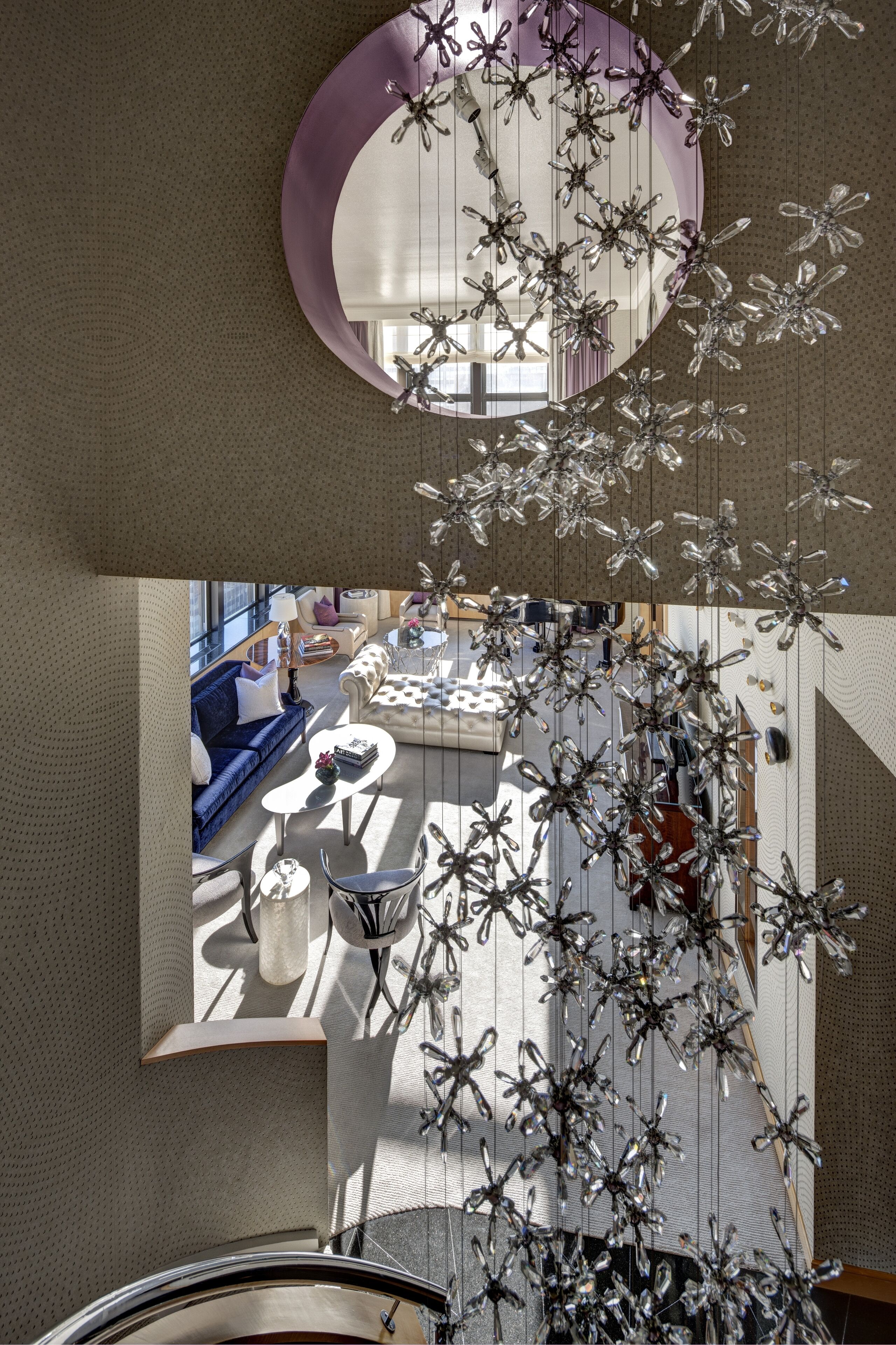 A modern interior with a circular mirror, a hanging metallic sculpture, and a seating area with sofas and tables.
